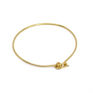 May include: A simple, gold-colored bangle bracelet. The bracelet is a complete circle with a clasp closure. The metal has a shiny finish. The bracelet is a minimalist jewelry piece.