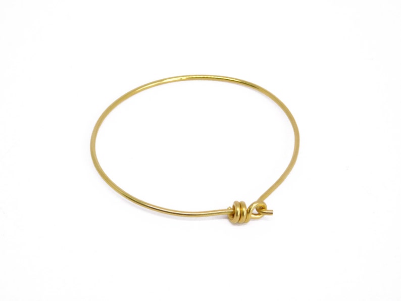 May include: A simple, gold-colored bangle bracelet. The bracelet is a complete circle with a clasp closure. The metal has a shiny finish. The bracelet is a minimalist jewelry piece.