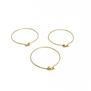 May include: Three gold-colored bangle bracelets with a knot design. The bracelets are circular and appear to be made of thin metal wire. They are set against a white background.