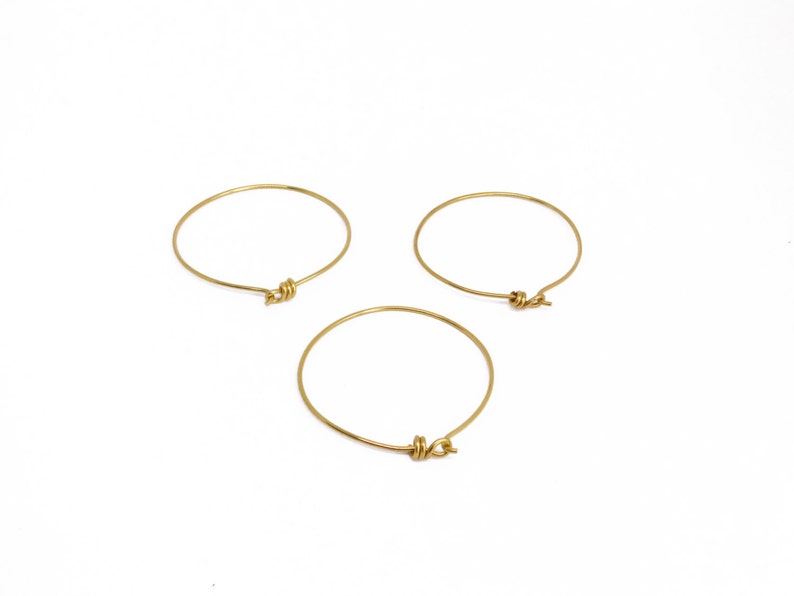 May include: Three gold-colored bangle bracelets with a knot design. The bracelets are circular and appear to be made of thin metal wire. They are set against a white background.