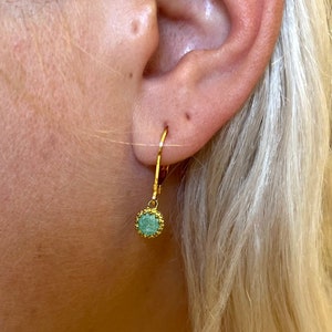 May include: Gold hoop earrings with a small, round, green gemstone pendant.