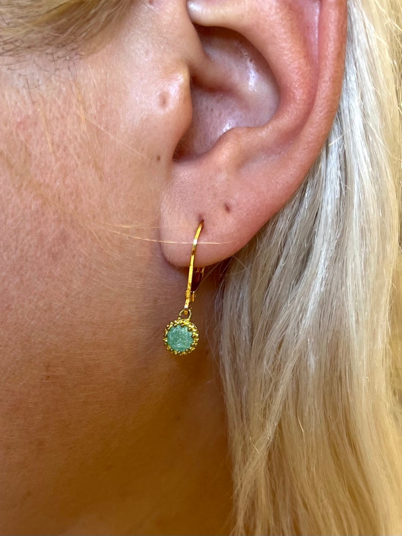 May include: Gold hoop earrings with a small, round, green gemstone pendant.
