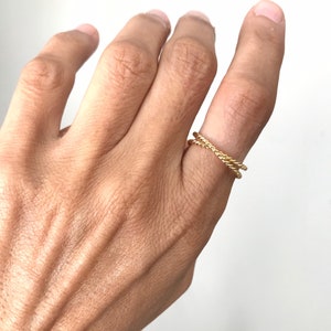 May include: A gold-toned, double-strand, twisted ring. The ring is worn on a finger.