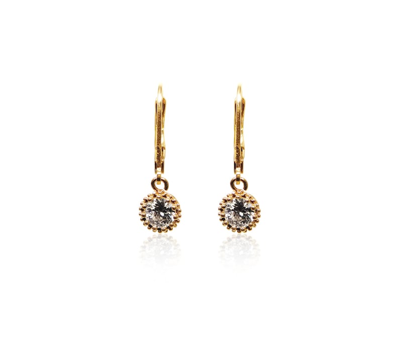 May include: A pair of gold dangle earrings with a small round clear stone set in a gold bezel.