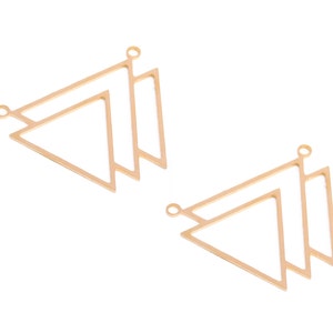 Pode incluir: Dois pingentes de triângulo de metal dourado com um laço na parte superior para prender em joias. Os triângulos são sobrepostos.