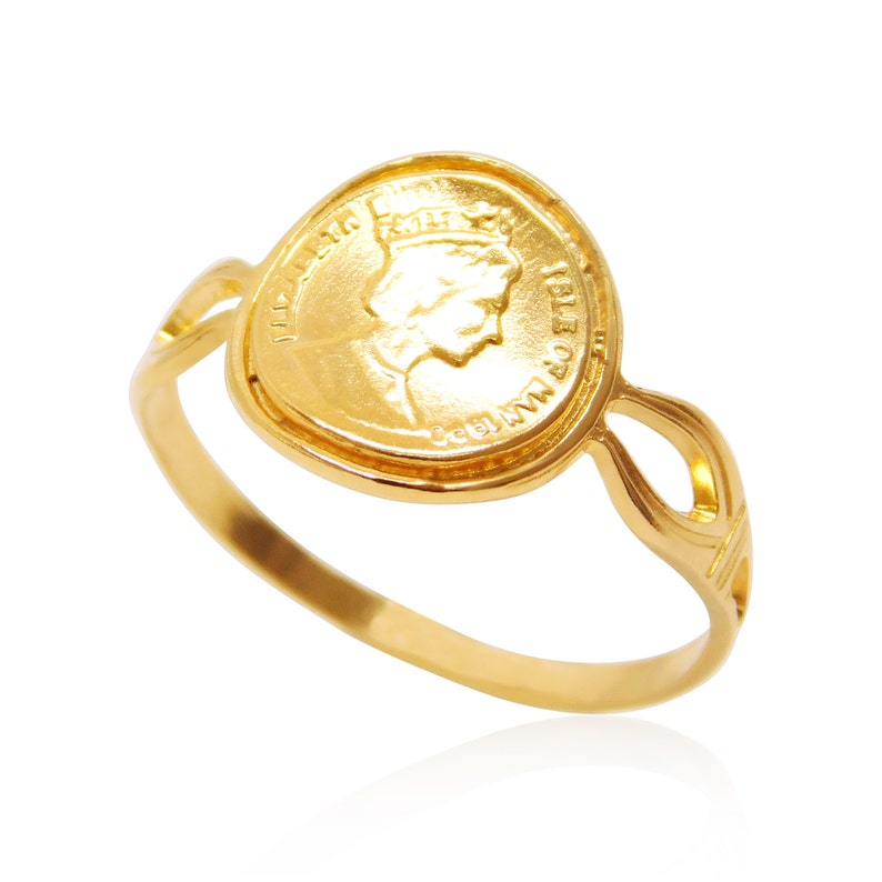 May include: A gold-colored ring featuring a coin design. The coin has a profile of a person and text around the edge. The ring band has an open design with decorative elements on the sides. The ring is set against a white background.