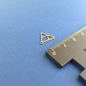 May include: A gold-colored metal triangle with a geometric design. The triangle has three small holes in the corners.