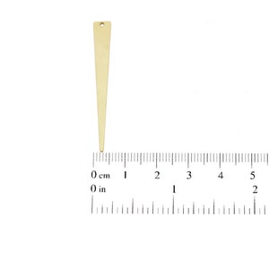 May include: A gold-colored metal triangle pendant with a hole at the top. The pendant is about 2 inches long and is measured against a ruler.