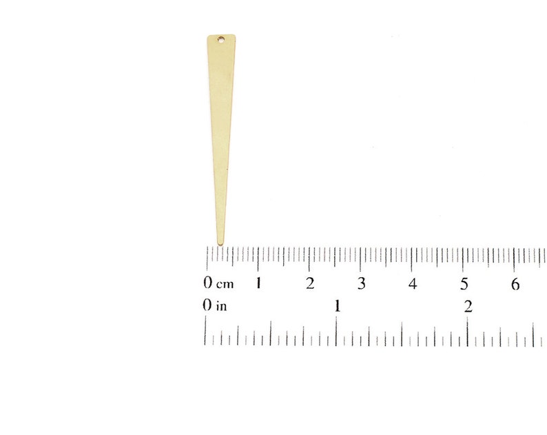 May include: A gold-colored metal triangle pendant with a hole at the top. The pendant is about 2 inches long and is measured against a ruler.