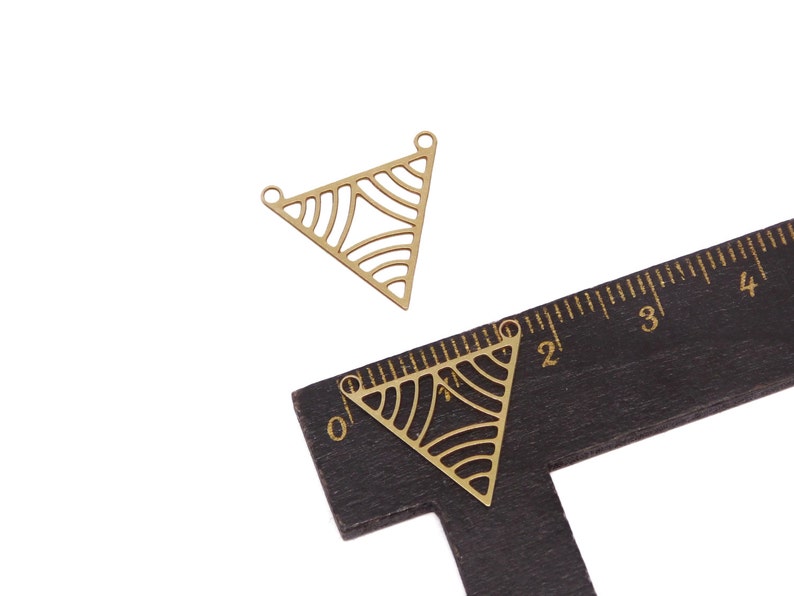 May include: Two gold-colored metal triangle pendant charms with a geometric pattern. The charms are approximately 2 inches in length.