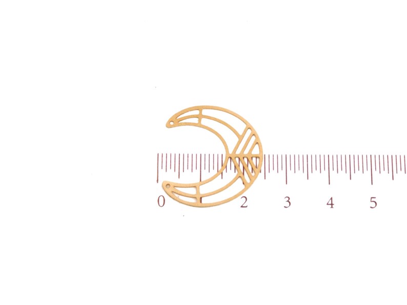 May include: A gold-colored, crescent moon-shaped charm with geometric cutouts. The charm has two small holes for attaching to jewelry. A ruler shows the charm is approximately 1 inch wide.