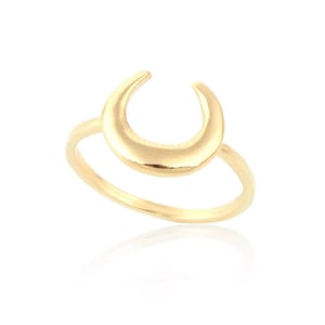 May include: A gold-colored ring featuring a crescent moon design. The ring has a smooth, polished finish and a delicate band. The moon shape is centered and slightly raised, creating a three-dimensional effect. The ring is set against a white background.