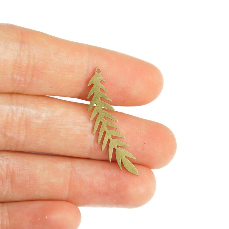 May include: A gold-colored metal leaf charm with a hole at the top for hanging. The leaf is detailed with a delicate, fern-like design.