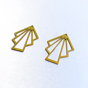 May include: A pair of gold-colored metal earrings with a geometric fan design. The earrings are made of thin metal and have a delicate, intricate design.