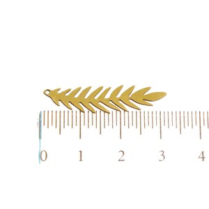 May include: A gold-colored metal leaf charm with a hole at the top for attaching to jewelry or other crafts. The charm is approximately 3 cm long and is shown next to a ruler.