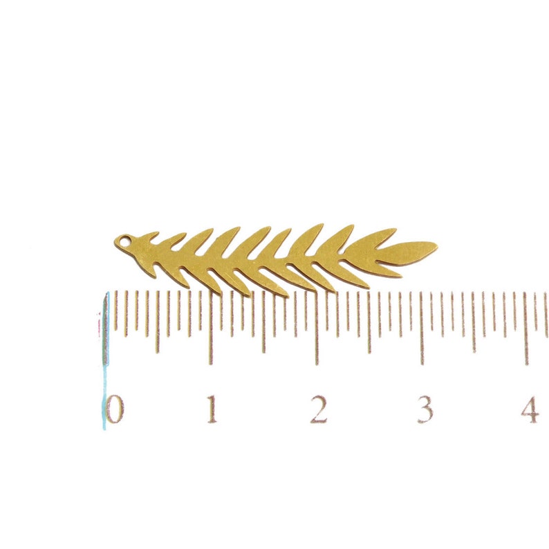 May include: A gold-colored metal leaf charm with a hole at the top for attaching to jewelry or other crafts. The charm is approximately 3 cm long and is shown next to a ruler.