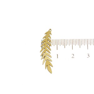 May include: A gold-colored metal leaf charm measuring approximately 1.5 inches in length. The charm is shaped like a fern leaf with a small hole at the top for attaching to jewelry or other crafts.