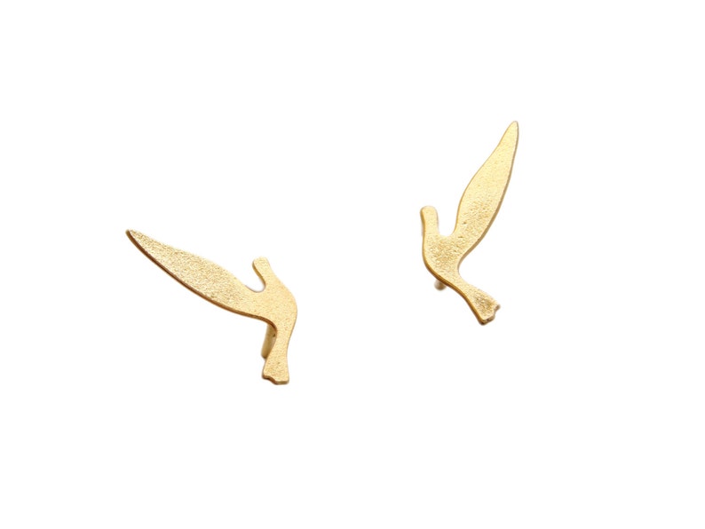 May include: A pair of gold-toned earrings shaped like flying birds.
