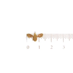 May include: A gold-colored bee charm with a striped pattern. The charm is about 1 inch long and is shown next to a ruler.