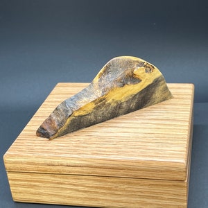 Könnte beinhalten: Eine Holzkiste mit einer natürlichen Holzoptik und einem einzigartigen, dunklen Holzdeckel. Der Deckel ist wellenförmig und hat ein natürliches, organisches Aussehen.