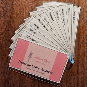 May include: A fan of cards with the names of different color seasons, including Deep Winter, Winter, Deep Autumn, Autumn, Summer, Light Summer, Bright Spring, Spring, Spring, and Light Spring. The cards are fanned out to reveal a pink card with the text "JenGirl Style find your glow Pantone Color Analysis Seasonal Color Analysis System".