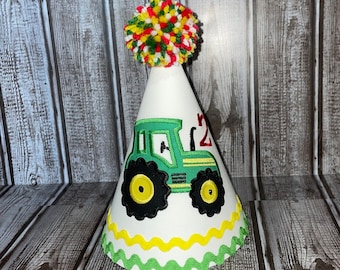 May include: Green and yellow tractor party hat with a red number 2 and a multi-colored pom-pom on top.