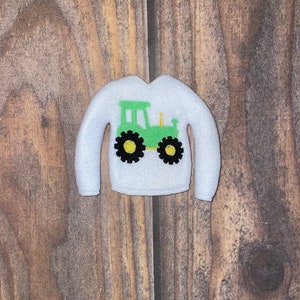 May include: White long-sleeved shirt with a green tractor design on the front.