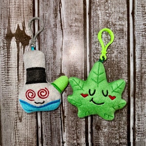 May include: Two plush keychains, one shaped like a green leaf with a smiling face and the other shaped like a white and blue character with a swirling eye design.