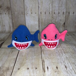 May include: Two plush shark toys, one blue and one pink, with embroidered eyes and teeth.