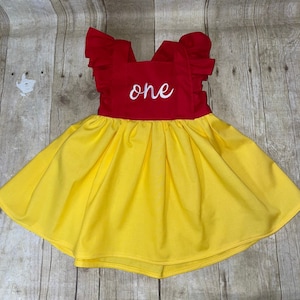 May include: A yellow and red sleeveless dress with a ruffled neckline and a white embroidered "one" on the red bodice.