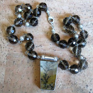 May include: A silver necklace with a pendant featuring a dendritic agate stone. The necklace is made with smoky quartz beads.
