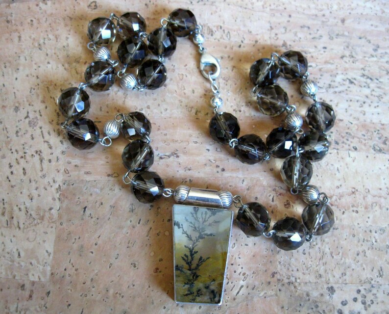 May include: A silver necklace with a pendant featuring a dendritic agate stone. The necklace is made with smoky quartz beads.