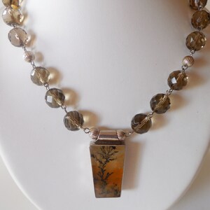 May include: A brown and clear crystal beaded necklace with a silver pendant featuring a dendritic agate stone.