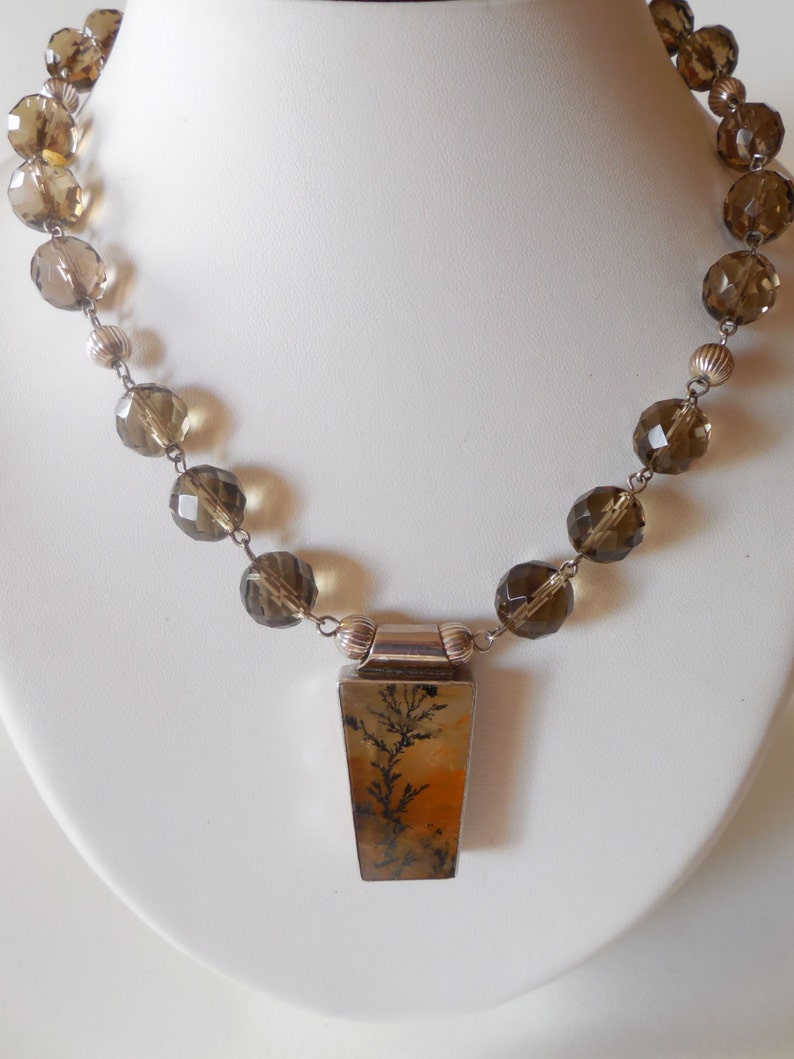 May include: A brown and clear crystal beaded necklace with a silver pendant featuring a dendritic agate stone.