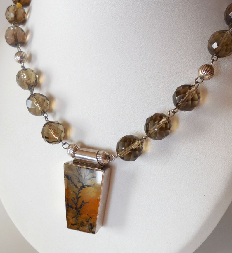 May include: A silver necklace with a brown and orange dendritic agate pendant and faceted brown glass beads.
