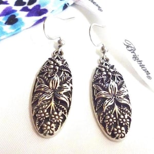 Pewter tone earrings with a raised floral design with a Brighton dustbag. They have a flower on in the center that looks like a lily. They have hook attachments.