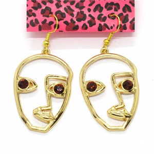 May include: Gold-tone earrings with a face outline design and brown rhinestone accents.