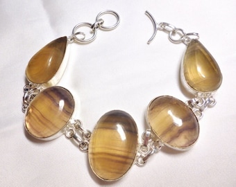 May include: A silver bracelet with five teardrop-shaped brown and yellow fluorite stones. The bracelet has a lobster clasp closure.