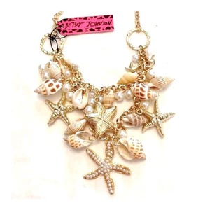 May include: Gold tone necklace with a charm of seashells and starfish. The necklace has a "Betsey Johnson" tag.