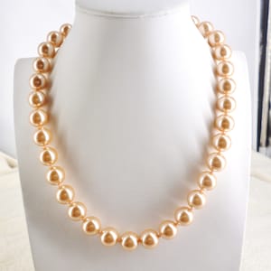 May include: A strand of large, round, peach-colored faux pearls on a white mannequin bust.