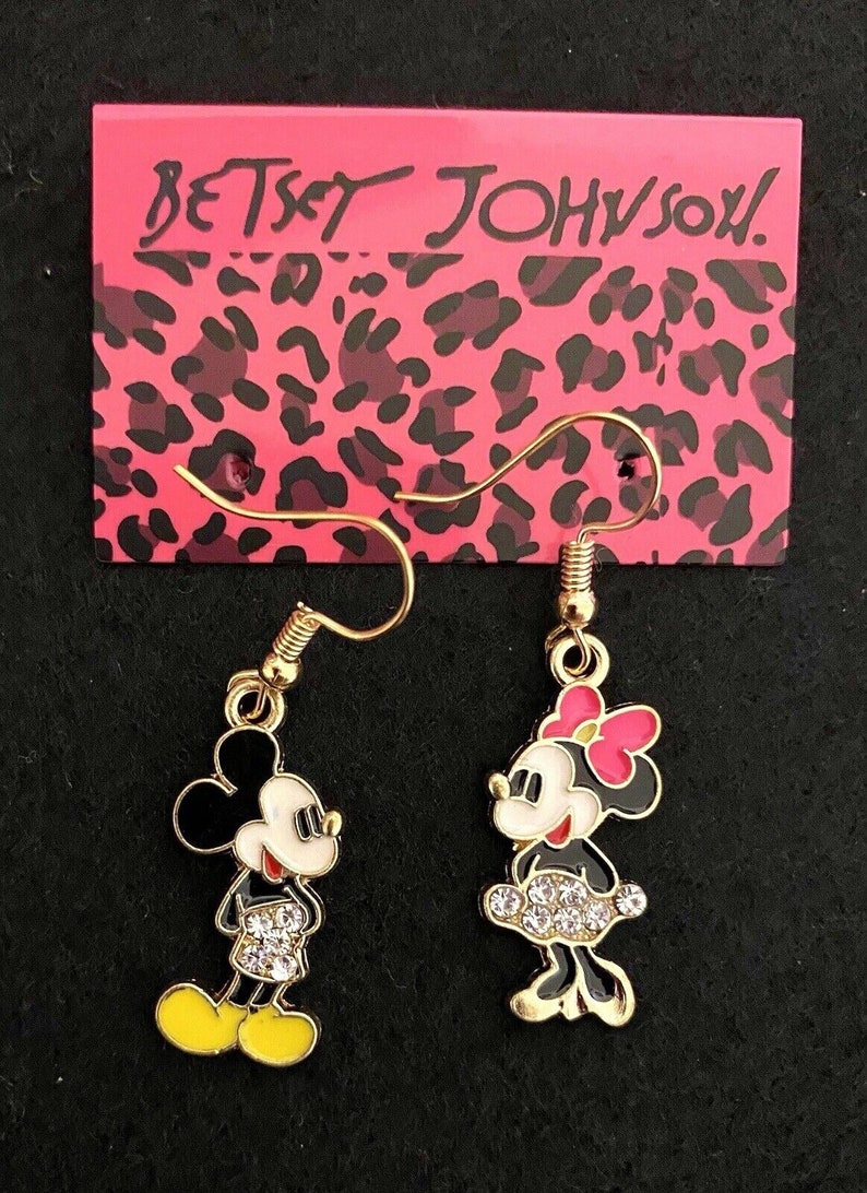 A pair of dangle hook earrings, one with a Mickey Mouse charm and the other with a Minnie Mouse charm. Minnie has a crystal encrusted skirt, Mickey's shorts are crystal encrusted. They are on a Betsey Johnson earring card.