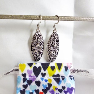 The earrings are hanging down, showing a raised floral design with a Brighton dustbag below; the bag has a bright multi colored heart design.