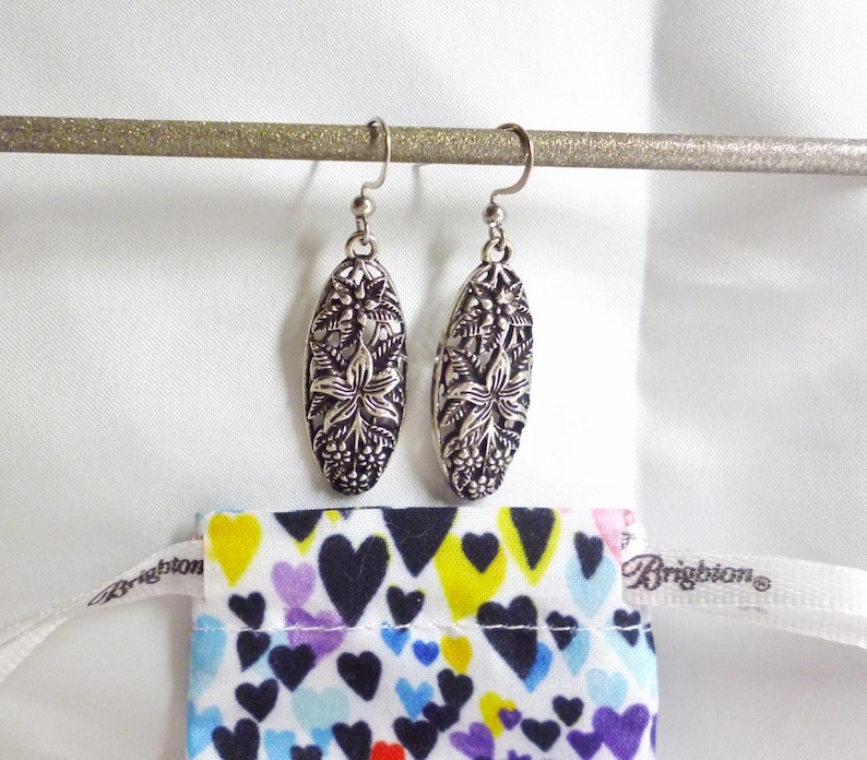 The earrings are hanging down, showing a raised floral design with a Brighton dustbag below; the bag has a bright multi colored heart design.