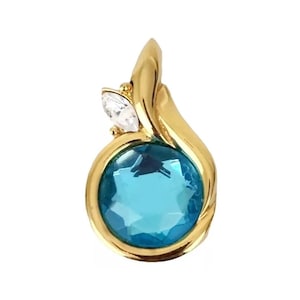 May include: A gold-toned pendant featuring a large, round, light blue gemstone. A smaller, clear, marquise-cut stone is set above the blue stone. The pendant has a flowing, organic design.