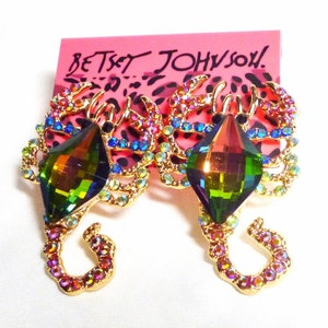 May include: A pair of gold-tone scorpion earrings with iridescent green crystal accents and multi-colored rhinestones. The earrings feature the text "BETSEY JOHNSON!" on the back.