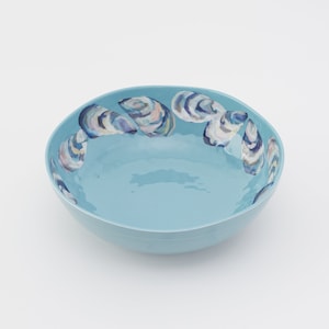 May include: A light blue ceramic bowl with a scalloped rim and a design of painted oyster shells around the edge.