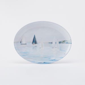 May include: A round decorative plate featuring a watercolor painting of sailboats on a calm sea. The plate has a glossy finish and a light blue and white color palette, evoking a nautical theme.