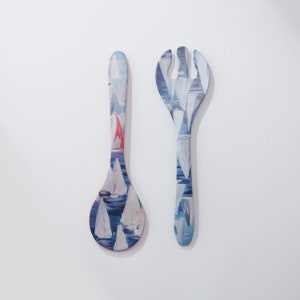 May include: A set of two wooden kitchen utensils with a blue and white sailboat design. The utensils are a spoon and a salad fork.