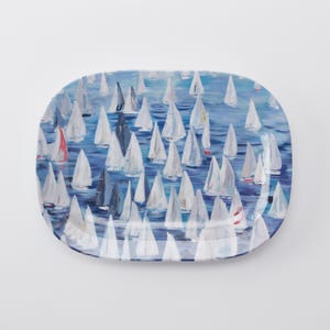 May include: An oval ceramic serving platter featuring a painted scene of numerous white sailboats on a blue sea. The artwork displays a dense collection of triangular sails in various shades of white, light blue, and grey, with small red accents.