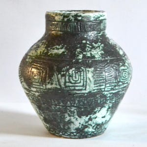 Pode incluir: Um pequeno vaso de cerâmica verde e preto com um padrão geométrico. O vaso tem um corpo arredondado e um pescoço estreito.